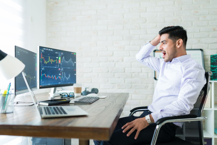 Shocked trader watching live charts of CFD trading commodities and CFD ETF trading losses on multiple monitors at home office.