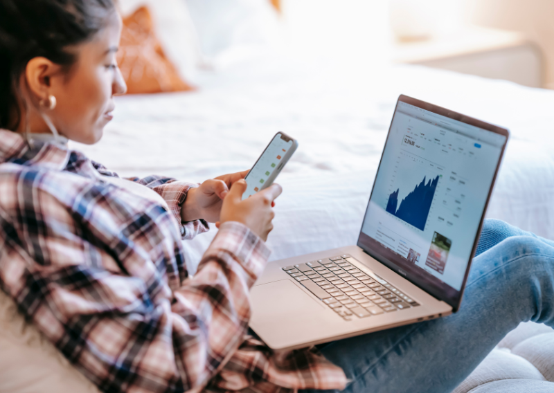 Young trader checking market charts on phone and laptop, discover how the best forex brokers empower flexible trading.