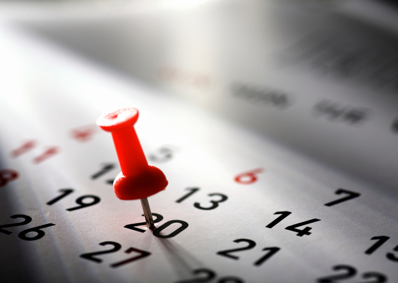 Red push pin marking an important financial date on a calendar for trading schedule or economic event